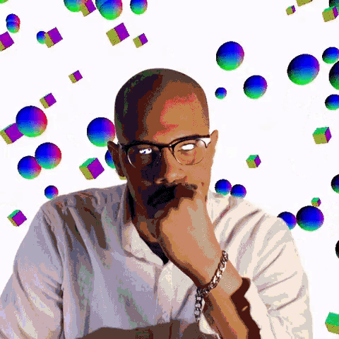 a man wearing glasses and a chain bracelet is surrounded by colorful balls and cubes