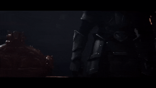 a person in a black armor is holding a sword in a dark room .