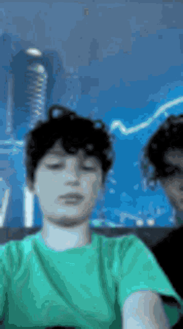 a boy in a green t-shirt is taking a selfie with another boy in a black shirt .