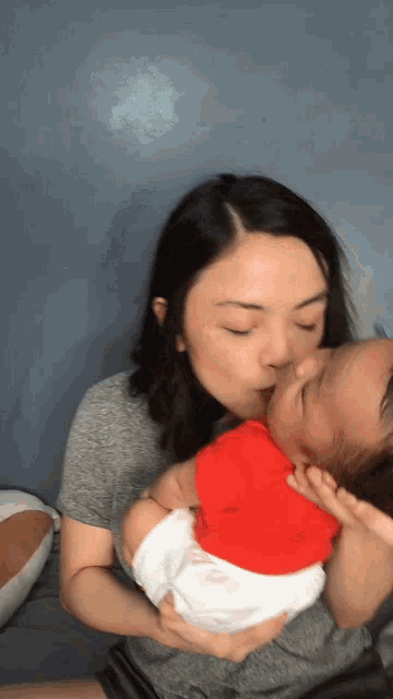 a woman is kissing a baby who is wearing a red and white shirt
