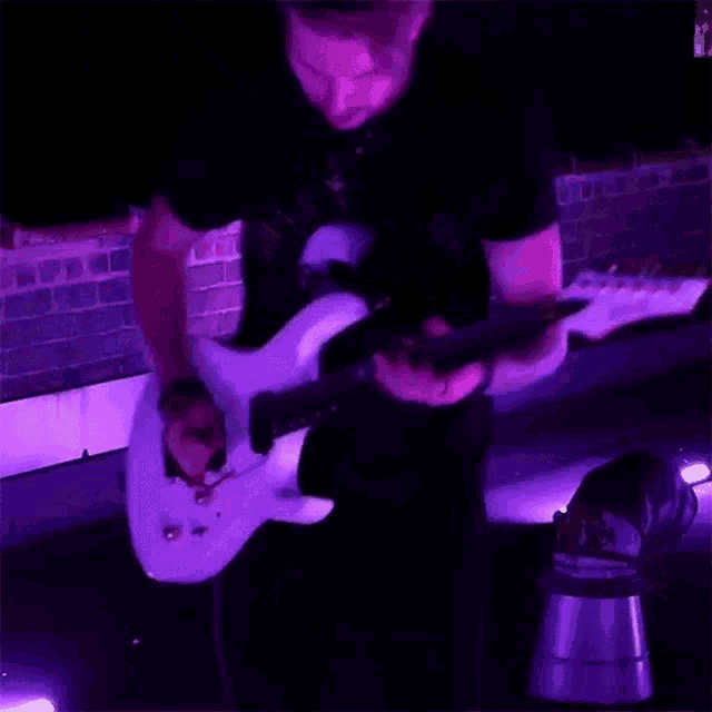 a man in a black shirt is playing a white guitar in a dark room