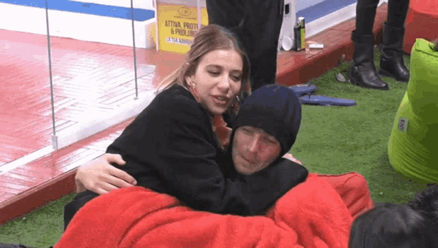 a woman is hugging a man who is wrapped in a red blanket with a sign in the background that says attiva prote