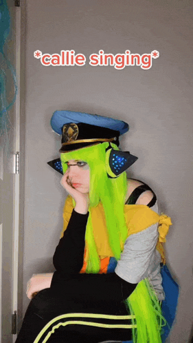 a girl with green hair and a police hat is sitting in front of a door with the words " callie singing " above her