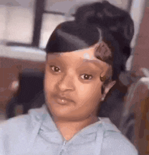 a little girl with a bun on her head is sitting in a chair making a funny face .