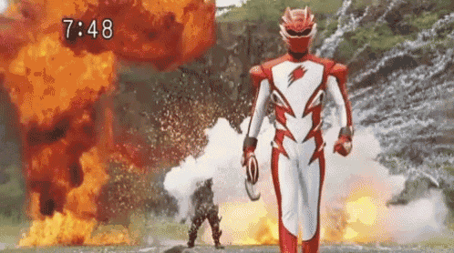 a red and white superhero is standing in front of a fire explosion .