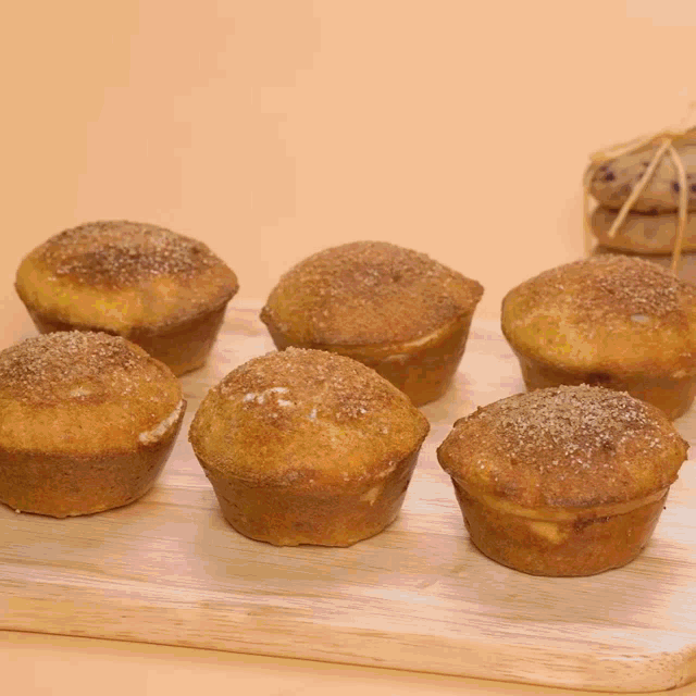 a wooden cutting board topped with muffins with sugar on top