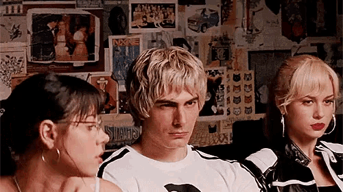 a man and two women are sitting in front of a wall with posters on it including one that says ' slums '