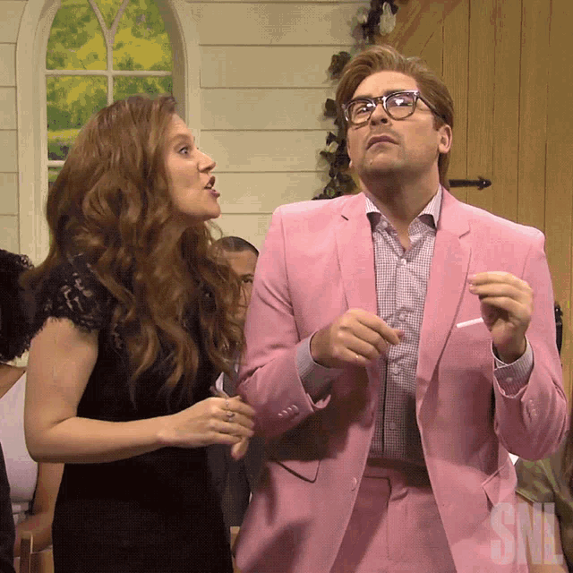 a man in a pink suit talks to a woman in a black dress