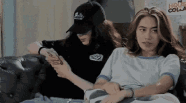 two women are sitting on a couch and one is looking at her phone