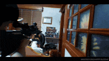a man holding a gun in a room with the words maverick ong happy buddha on the bottom right