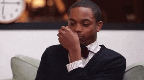 a man in a suit and bow tie is sitting on a couch and covering his nose with his hand .
