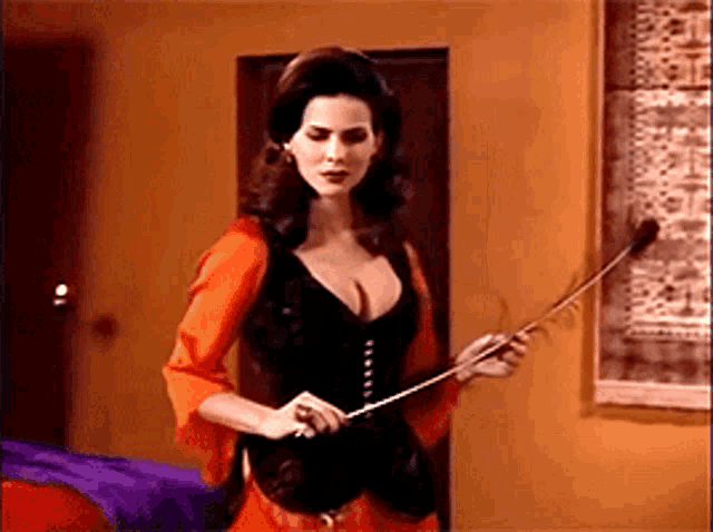a woman in a black corset is holding a whip in her hand .
