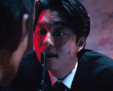 a man with blood on his face is holding a gun to his mouth .