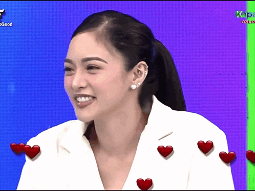 a woman in a white jacket is smiling with hearts around her on a screen that says kapamilya online