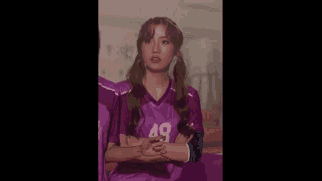 a girl in a purple soccer jersey is standing next to another girl with her arms crossed .