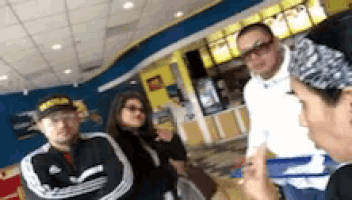 a group of people standing in a restaurant with one wearing a hat that says hawks on it