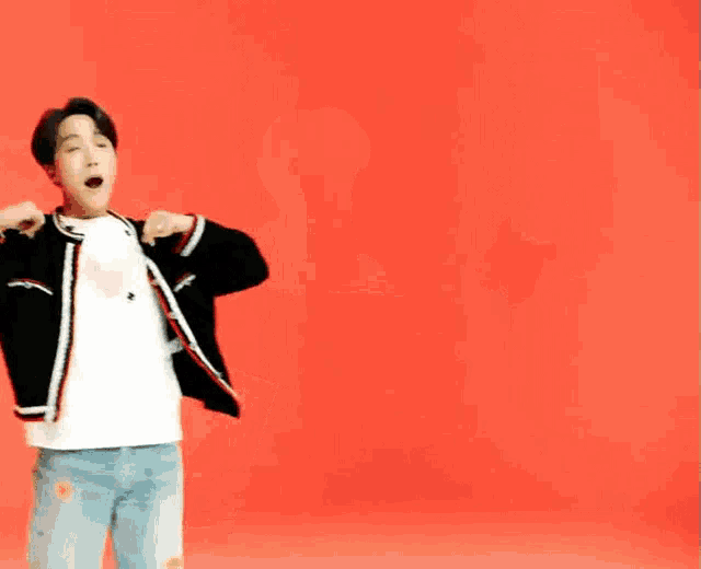 a man in a black jacket and white shirt is dancing with his arms outstretched against a red background .
