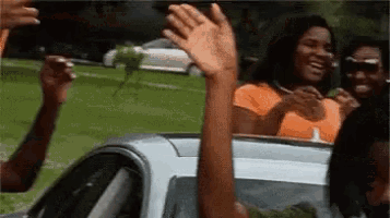 a group of people are waving their hands in the air while sitting in a car .