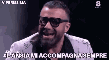 a man with a beard wearing sunglasses and a suit is making a funny face on a tv show .