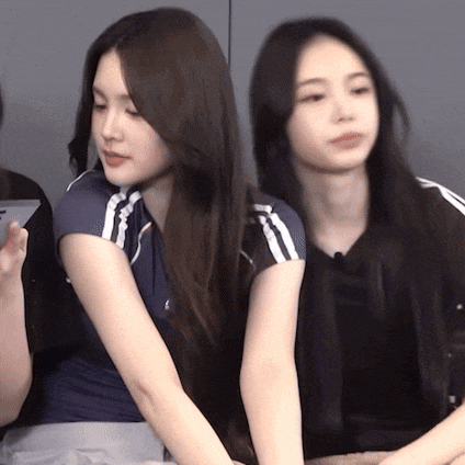 two women with long hair are sitting next to each other and one is holding a cell phone