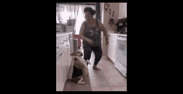 a woman is dancing in a kitchen with a dog standing next to her .