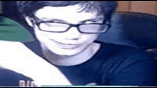 a young boy wearing glasses and a black shirt is smiling while looking at a piece of paper .