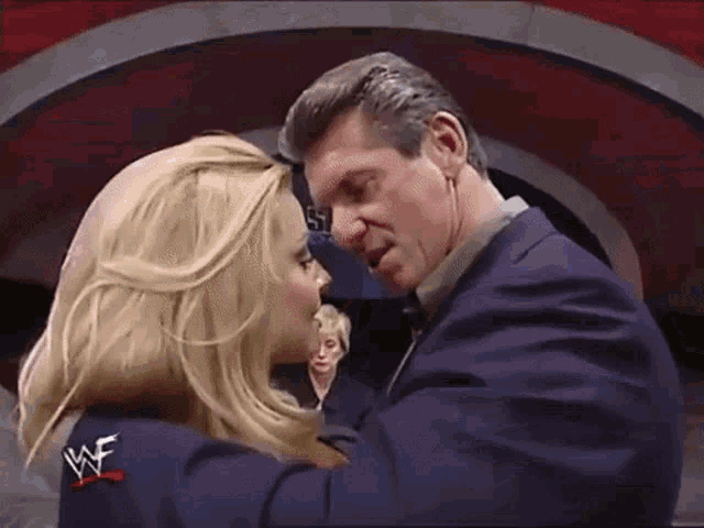 a man and a woman are kissing in front of a sign that says wwe on it .