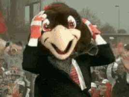a mascot wearing gloves and a suit stands in front of a crowd with a sign that says home depot