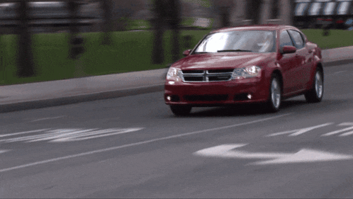 a red dodge car is driving down a city street