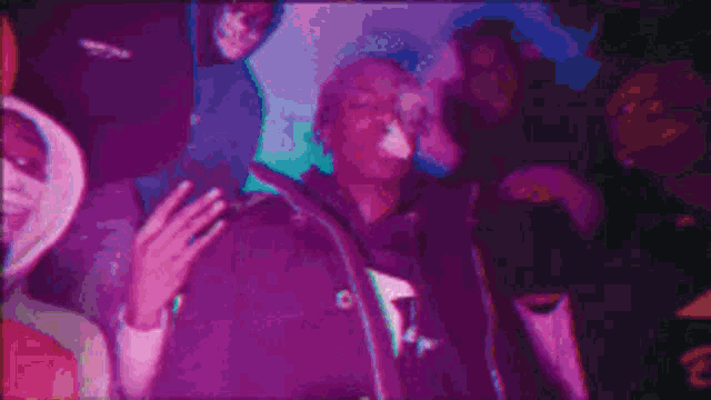 a man in a purple jacket is smoking a cigarette in a crowd .