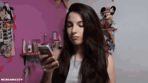 a girl is looking at her cell phone in front of a pink wall