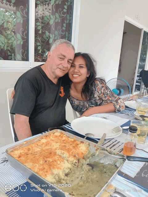 a man and woman sitting at a table with a casserole dish in front of them and the words shot on vivo camera on the bottom