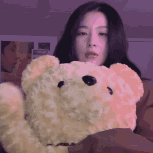 a woman is holding a teddy bear with a purple background