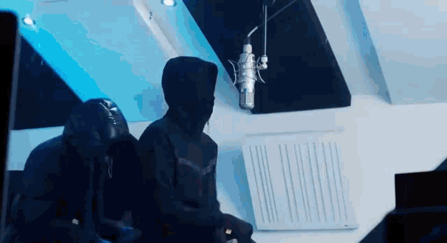a man in a hooded jacket is sitting in front of a microphone in a room .