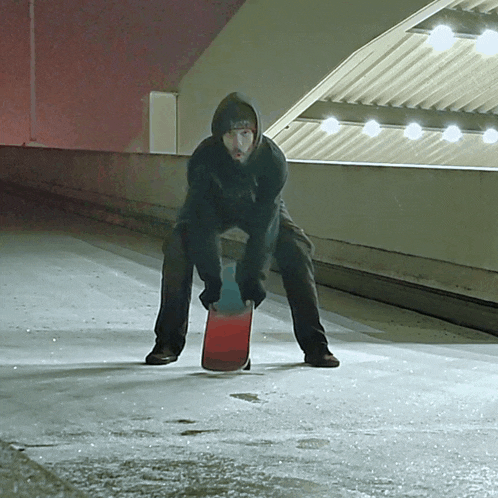 a man in a black hoodie is holding a red skateboard and wearing a beanie that says ' supreme '