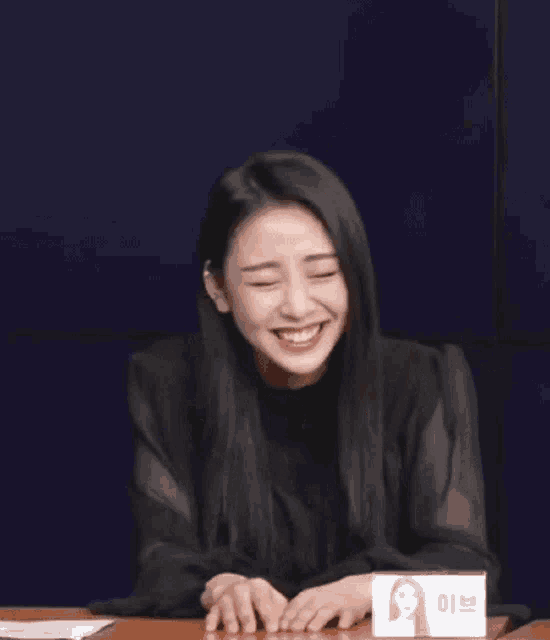 a woman in a black dress is sitting at a table with a box of tissues .