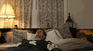 a man is laying on a bed with a lamp and a picture of a boat on the wall