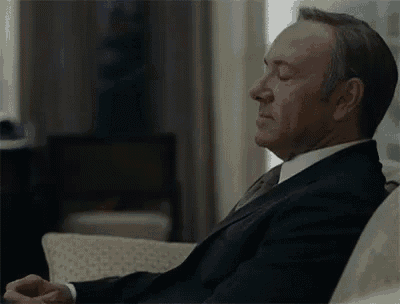 a man in a suit and tie is sitting on a couch with his eyes closed and his hands folded .