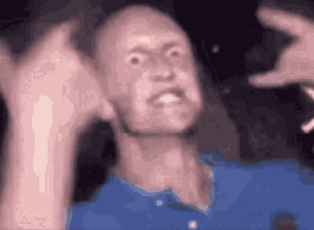 a man in a blue shirt is making a funny face with his hands up .