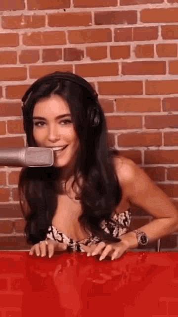 a woman wearing headphones is sitting at a red table with a microphone in front of a brick wall .