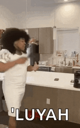 a woman in a white dress is standing in a kitchen with a man in a white shirt .