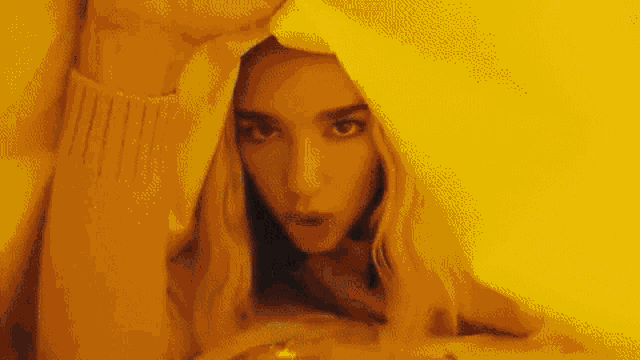 a woman is laying under a yellow blanket and looking out from underneath it .