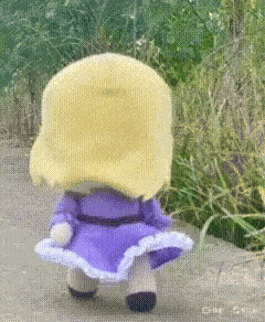 a stuffed doll with blonde hair and a purple dress is walking on a sidewalk