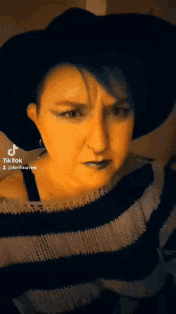 a woman wearing a black hat and a black and white striped sweater has a tiktok icon on her face