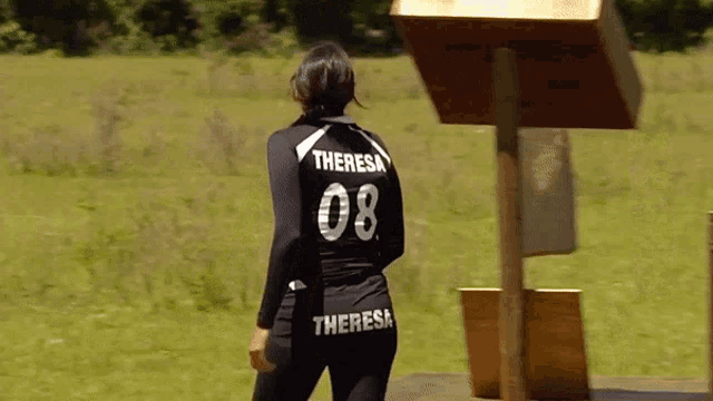a woman wearing a theresa 08 jersey stands in a grassy field
