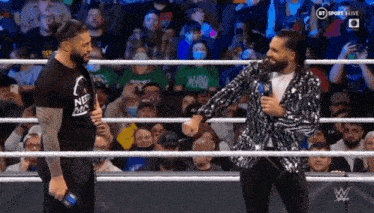 two men are standing next to each other in a wrestling ring talking to each other .
