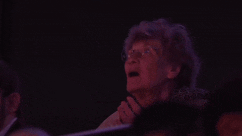 an elderly woman wearing glasses is sitting in a crowd of people watching a show .