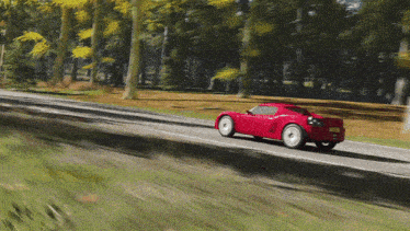 a red sports car is driving down a road with trees on the side