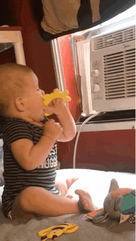a baby wearing a striped shirt that says ' the north face ' on it chews on a yellow toy