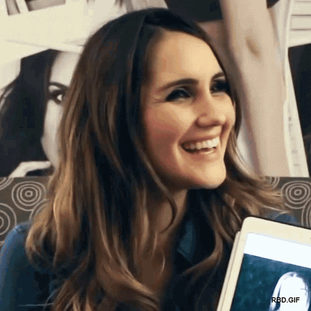a woman is smiling and holding a tablet with a picture of a woman on the screen